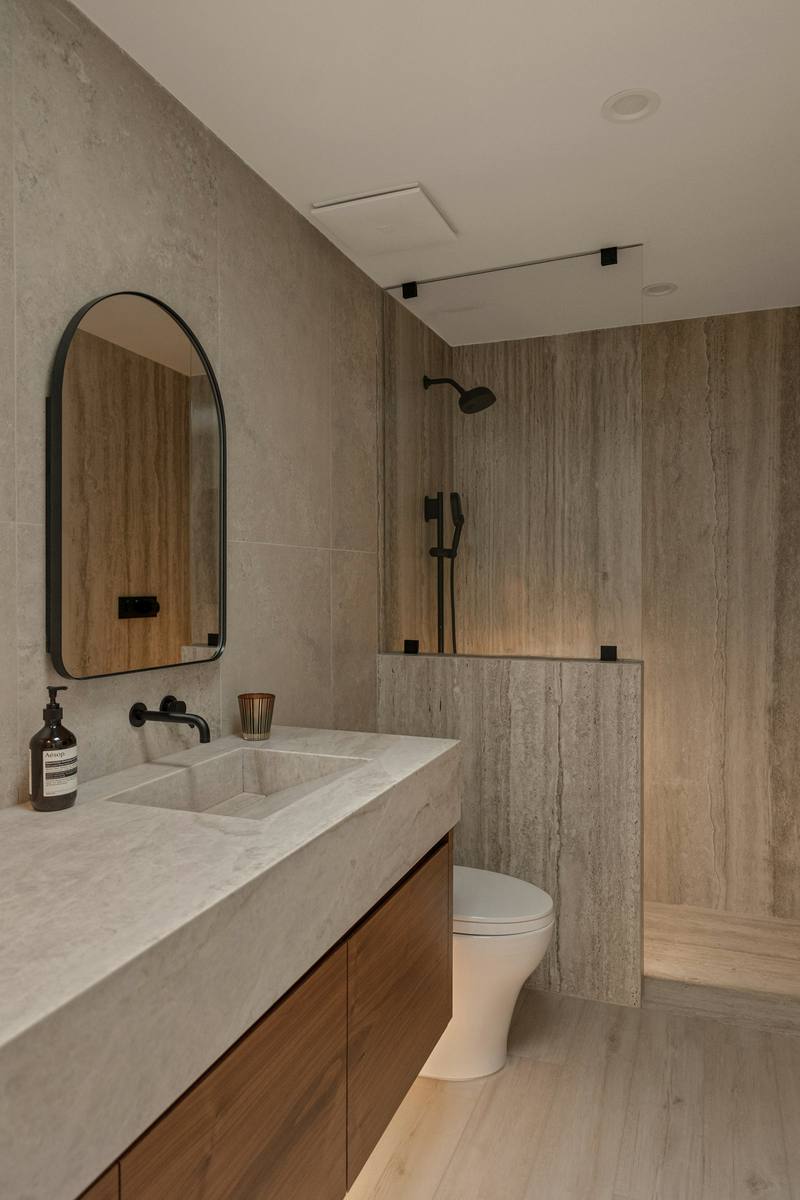 Bodengleiche Dusche mit Natursteinfliesen, Holzwaschtisch und rundem Spiegel